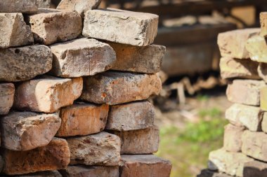 Duvarın köşesinde eski kırmızı tuğlalar ve arka planda yeşil çimenler var.