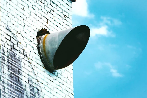 Air conditioning tube cut in diagonal sticking out of the white brick wall on blue sky with white clouds