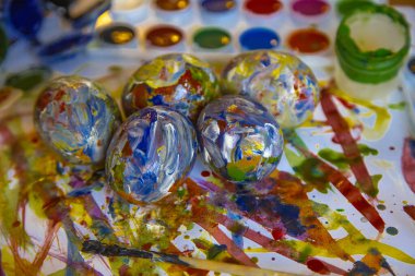 Paskalya renkli yumurtalar parlak beyaz bir zemin üzerinde uzanır, boyalarla ve resovaniya için fırçalarla çevrili. Parlak Paskalya yumurtaları, yan görünüş.