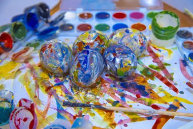 Paskalya renkli yumurtalar parlak beyaz bir zemin üzerinde uzanır, boyalarla ve resovaniya için fırçalarla çevrili. Parlak Paskalya yumurtaları, yan görünüş.