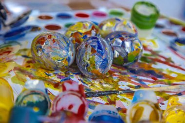 Paskalya renkli yumurtalar parlak beyaz bir zemin üzerinde uzanır, boyalarla ve resovaniya için fırçalarla çevrili. Parlak Paskalya yumurtaları, yan görünüş.