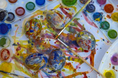 Paskalya renkli yumurtalar boyaların ve fırçaların arasında ayrı olarak uzanır parlak beyaz arka planda, parlak Paskalya yumurtaları, üstten görünen bir manzara.