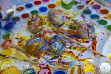 Paskalya renkli yumurtalar boyaların ve fırçaların arasında ayrı olarak uzanır parlak beyaz arka planda, parlak Paskalya yumurtaları, üstten görünen bir manzara.