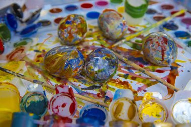 Paskalya renkli yumurtalar boyaların ve fırçaların arasında ayrı olarak uzanır parlak beyaz arka planda, parlak Paskalya yumurtaları, üstten görünen bir manzara.