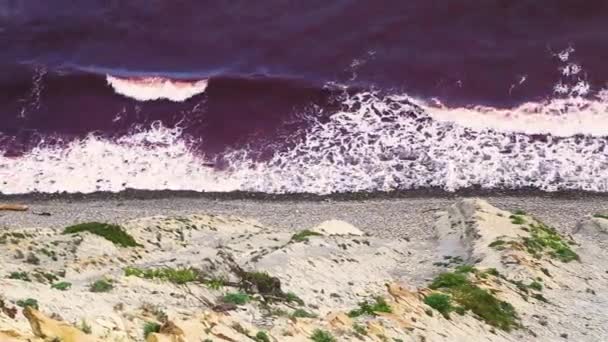 Vlny načervenalé barvy z řas bijí do skály s bílou pěnou — Stock video