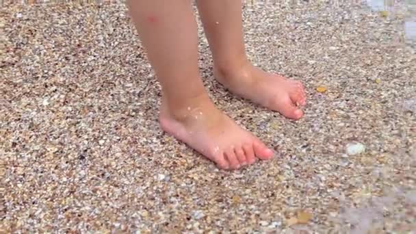 Las piernas de los niños están de pie sobre la arena y periódicamente — Vídeo de stock