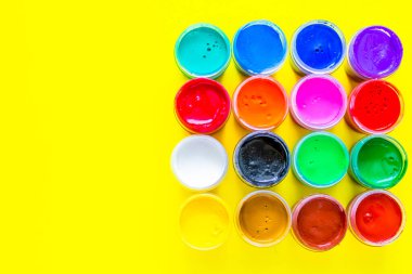 Birçok parlak boya kutusu sarı bir arka planda metin için bir yer ile birlikte duruyor. Üst görünüm, düz görünüm, kopyala boşluk, izole et.