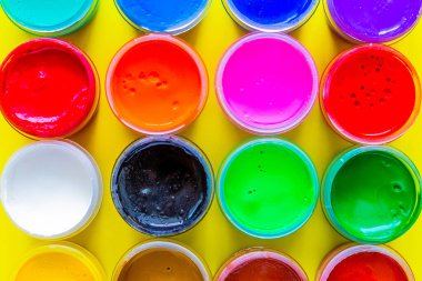 Birçok parlak boya kutusu sarı bir arka planda yan yana duruyor. Üst görünüm, düz görünüm, kopyala boşluk, izole et.