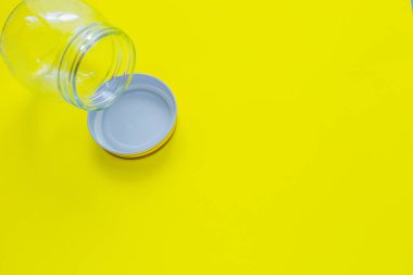 Sarı arka planda üst köşede kapaklı cam bir kavanoz var. Üst görünüm, düz görünüm, kopyala boşluk, izole et