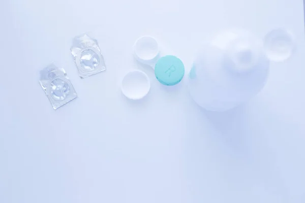 Bir lens çıkarıcı, bir lens saklama kabı ve beyaz arka plandaki fotoğrafın üzerinde iki kontakt lens var. Üst görünüm, düz görünüm, kopyala boşluk, izole et