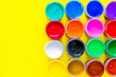 Birçok parlak boya kutusu sarı bir arka planda metin için bir yer ile birlikte duruyor. Üst görünüm, düz görünüm, kopyala boşluk, izole et.