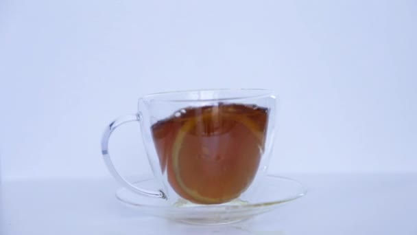 Una taza de té negro está sobre un fondo blanco, un anillo de limón amarillo se lanza en él, salpica. — Vídeos de Stock