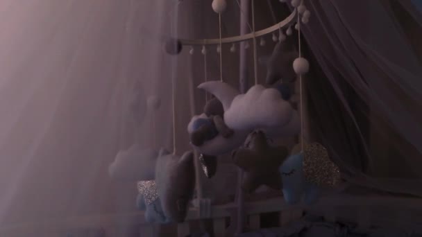 A childrens mobile with a month, clouds, stars and animals installed under the canopy over the crib is spinning, the light is evening, side view.. — Stock Video