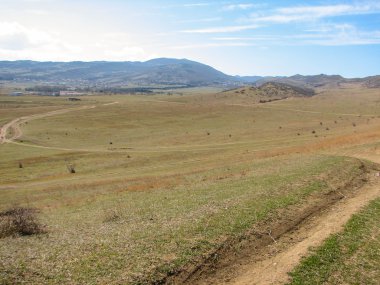 Açık mavi gökyüzü altında sarı çim kaplı tepe