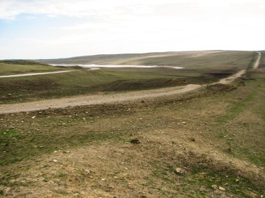 Açık mavi gökyüzü altında sarı çim kaplı tepe