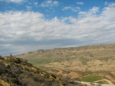 Açık mavi gökyüzü altında sarı çim kaplı tepe