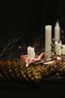 Mum ışığında pembe Noel süslemeleri, pembe kurdeleler, dallar, kuru çimenler, parlak mücevherler, kurdeleler ve çam kozalakları, siyah arka planda..