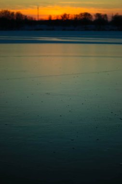 Donmuş gölde gün batımı. Sazlıklar ve ağaçlar, kıyılarda kar.
