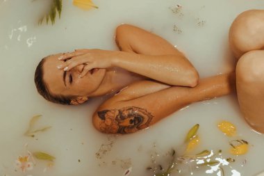 Güzel bir kız banyoda, çiçekli, yapraklı, sütlü suyla uzanıyor, narin bir genç kadın, açık arkaplan fotokopisinde şehvetli bir şekilde poz veriyor.