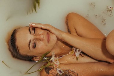 Güzel bir kız banyoda, çiçekli, yapraklı, sütlü suyla uzanıyor, narin bir genç kadın, açık arkaplan fotokopisinde şehvetli bir şekilde poz veriyor.