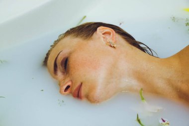 Güzel bir kız banyoda, çiçekli, yapraklı, sütlü suyla uzanıyor, narin bir genç kadın, açık arkaplan fotokopisinde şehvetli bir şekilde poz veriyor.