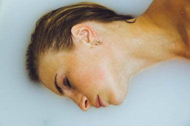 Güzel bir kız banyoda, çiçekli, yapraklı, sütlü suyla uzanıyor, narin bir genç kadın, açık arkaplan fotokopisinde şehvetli bir şekilde poz veriyor.