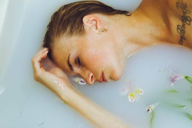 Güzel bir kız banyoda, çiçekli, yapraklı, sütlü suyla uzanıyor, narin bir genç kadın, açık arkaplan fotokopisinde şehvetli bir şekilde poz veriyor.