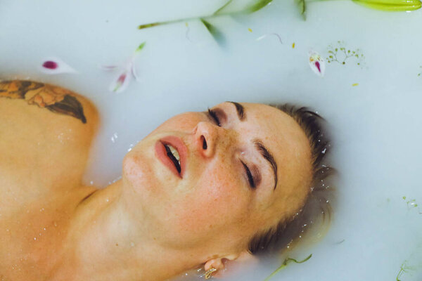 красивая девушка лежит в ванне с молочной водой с цветами и листьями, спа нежная молодая женщина позирует чувственно трогательный на светлом фоне копия пространства крупным планом портрет