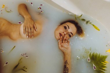 Süt, sarı çiçekler ve yapraklarla banyo yapan çekici çıplak kız. Spa vücut bakımı. Şefkat, güzellik ve özen. Dinlenme ve rahatlama zamanı..