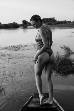 Güzel bir genç kadının mayolu portresi. Güzel bir atletik vücut, gölün yanında, bir teknede, siyah beyaz bir fotoğraf.