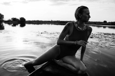 Güzel bir genç kadının mayolu portresi. Güzel bir atletik vücut, gölün yanında, bir teknede, siyah beyaz bir fotoğraf.