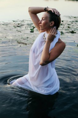 Suda genç ve güzel bir kadının portresi, çilli ve yeşil gözlü. Güzel gün batımı ışığı. Atletik cisim, gölün yanında, suyun arka planında.