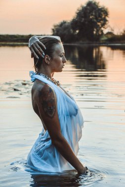 Suda genç ve güzel bir kadının portresi, çilli ve yeşil gözlü. Güzel gün batımı ışığı. Atletik cisim, gölün yanında, suyun arka planında.