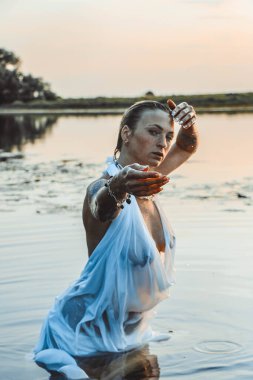 Suda genç ve güzel bir kadının portresi, çilli ve yeşil gözlü. Güzel gün batımı ışığı. Atletik cisim, gölün yanında, suyun arka planında.