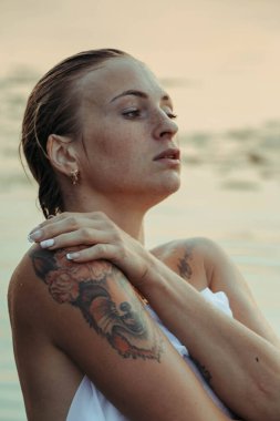 Suda genç ve güzel bir kadının portresi, çilli ve yeşil gözlü. Güzel gün batımı ışığı. Atletik cisim, gölün yanında, suyun arka planında.