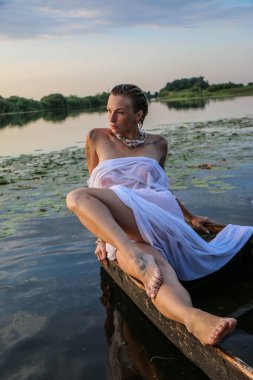 Suda genç ve güzel bir kadının portresi, çilli ve yeşil gözlü. Güzel gün batımı ışığı. Atletik cisim, gölün yanında, suyun arka planında.