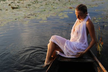 Güzel bir genç kadının portresi, çilli ve yeşil gözlü. Güzel bir gün batımı ışığı. Atletik cisim, bir teknede, suyun arka planında.