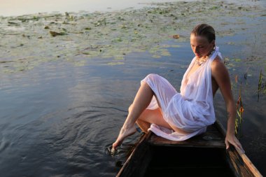 Güzel bir genç kadının portresi, çilli ve yeşil gözlü. Güzel bir gün batımı ışığı. Atletik cisim, bir teknede, suyun arka planında.