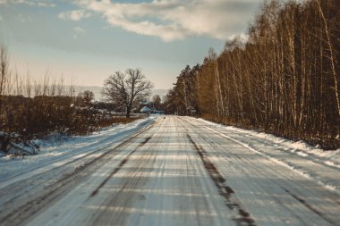 Güzel kış manzarası ağaçların arasındaki beyaz yol, mavi gökyüzü bulutlu güneşli gün, hepsi karda, ılık günbatımı ışığı