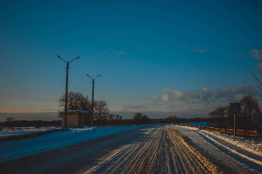 Güzel kış manzarası ağaçların arasındaki beyaz yol, mavi gökyüzü bulutlu güneşli gün, hepsi karda, ılık günbatımı ışığı