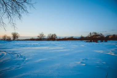 Güzel kış manzarası, bulutlu gün batımı, uzaktaki orman, kardaki tarla ve ağaçlar, dondurucu güneşli bir akşam, Ukrayna
