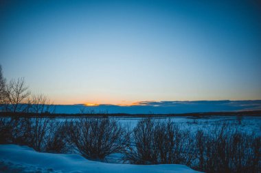 Güzel kış manzarası, bulutlu gün batımı, uzaktaki orman, kardaki tarla ve ağaçlar, dondurucu güneşli bir akşam, Ukrayna