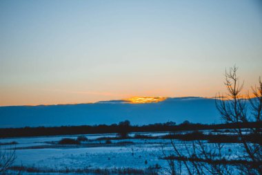 Güzel kış manzarası, bulutlu gün batımı, uzaktaki orman, kardaki tarla ve ağaçlar, dondurucu güneşli bir akşam, Ukrayna