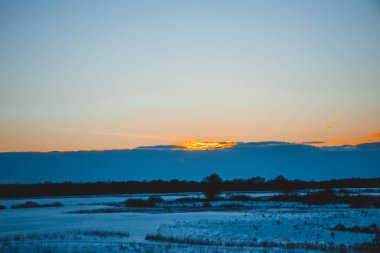 Güzel kış manzarası, bulutlu gün batımı, uzaktaki orman, kardaki tarla ve ağaçlar, dondurucu güneşli bir akşam, Ukrayna