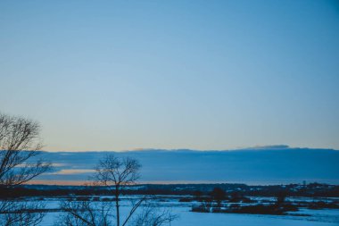 Güzel kış manzarası, bulutlu gün batımı, uzaktaki orman, kardaki tarla ve ağaçlar, dondurucu güneşli bir akşam, Ukrayna