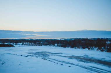 Güzel kış manzarası, bulutlu gün batımı, uzaktaki orman, kardaki tarla ve ağaçlar, dondurucu güneşli bir akşam, Ukrayna