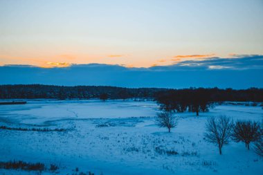 Güzel kış manzarası, bulutlu gün batımı, uzaktaki orman, kardaki tarla ve ağaçlar, dondurucu güneşli bir akşam, Ukrayna