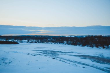 Güzel kış manzarası, bulutlu gün batımı, uzaktaki orman, kardaki tarla ve ağaçlar, dondurucu güneşli bir akşam, Ukrayna