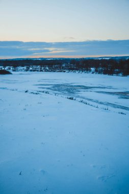 Güzel kış manzarası, bulutlu gün batımı, uzaktaki orman, kardaki tarla ve ağaçlar, dondurucu güneşli bir akşam, Ukrayna