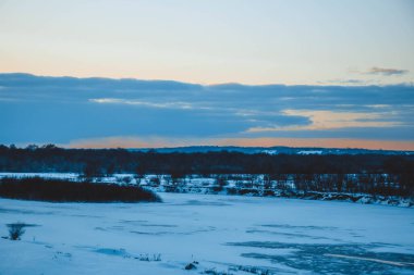 Güzel kış manzarası, bulutlu gün batımı, uzaktaki orman, kardaki tarla ve ağaçlar, dondurucu güneşli bir akşam, Ukrayna